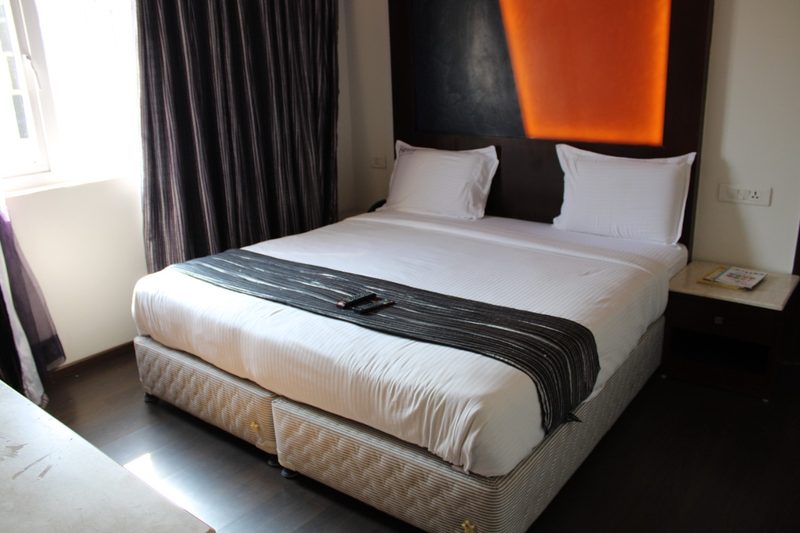 Double bed with a dark runner, bedside table and curtained window